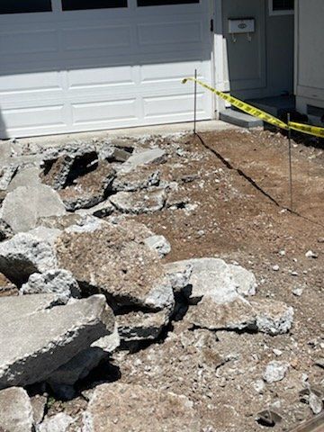 Debris from demolished concrete on a driveway in front of a white garage door, with caution tape.