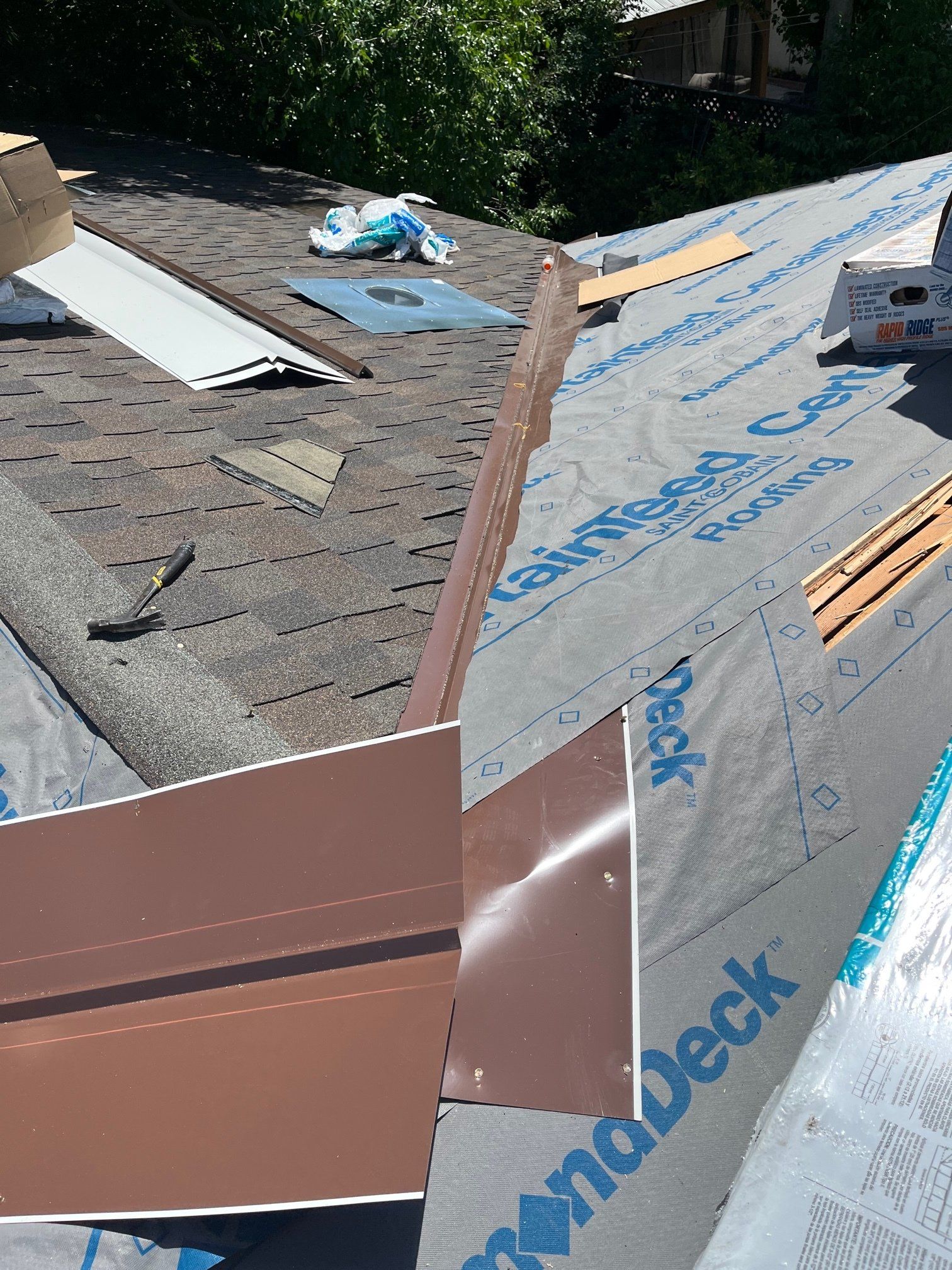 Roofing work: brown metal flashing installed on a roof with gray shingles and blue underlayment.