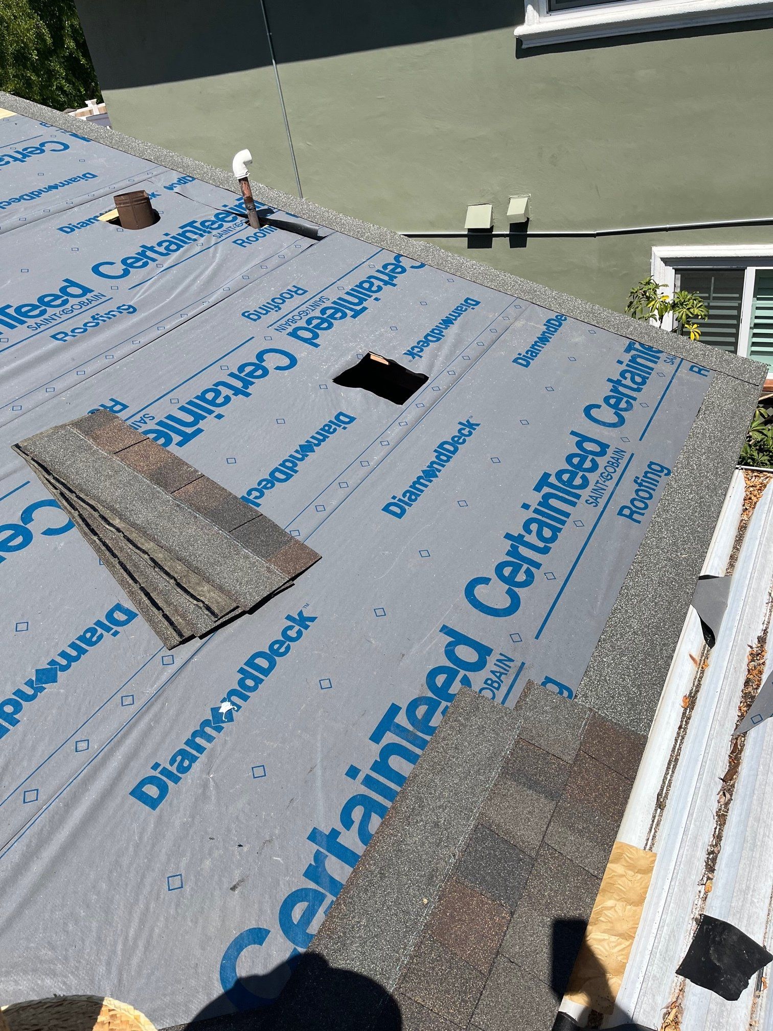 Roofing shingles being installed on a house, with exposed underlayment and a hole in the roof.