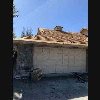 Garage with partially removed brown roof tiles under a blue sky.