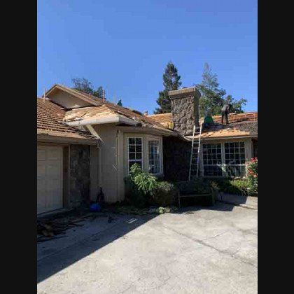 Roofers working on a house with removed shingles, ladder, stone chimney, blue sky.