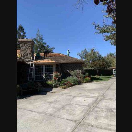 Workers on a roof, removing old tiles, with ladder and stone chimney. Sunny day.