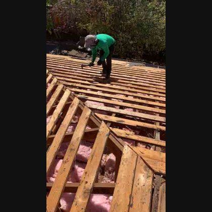 A person in green clothing on a rooftop removing old wooden planks.