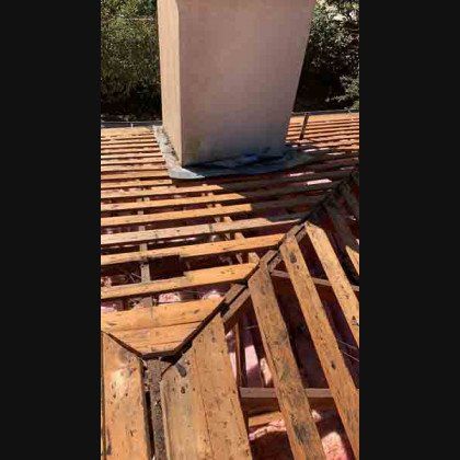 Roof being repaired; damaged wood framing around a chimney, exposed insulation.