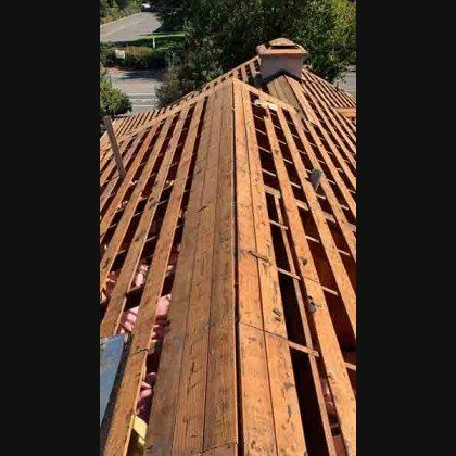 View from above of wooden roof beams with exposed insulation and chimney.