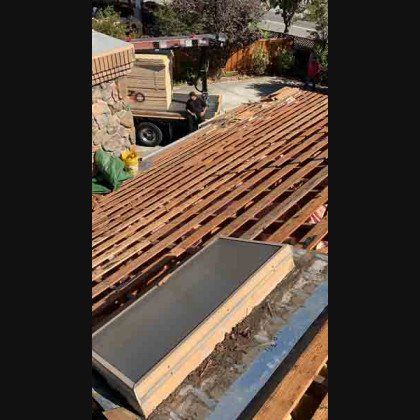 Roof partially dismantled, a skylight is visible. Truck with materials in the background. Sunny day.