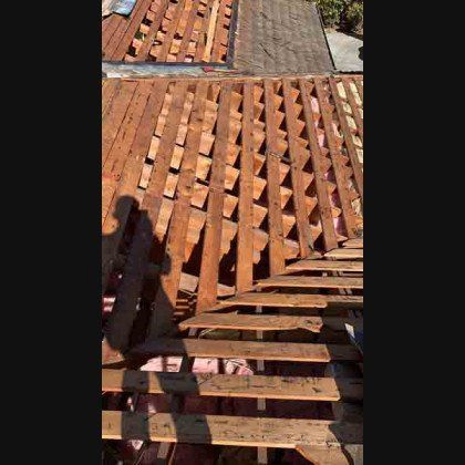 Overhead view of a roof under construction. Wooden beams and missing shingles are visible.