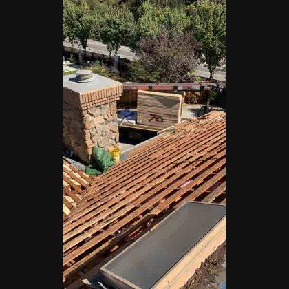 Rooftop view of a home undergoing construction. Wooden framework, chimney, and building materials are visible.