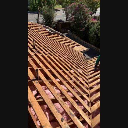 Roof under construction with exposed wooden framework, pink insulation, and a person working.
