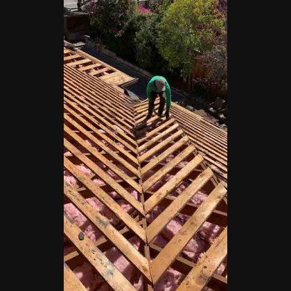 Person on a roof with wooden beams, working on a construction project, outdoors.