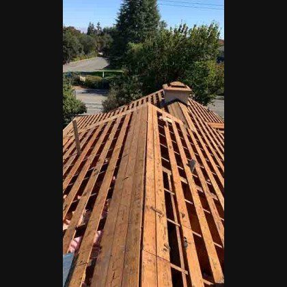 View of a partially constructed roof with exposed rafters, chimney, and neighborhood in the background.