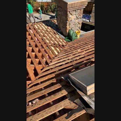 Roof under construction, showing exposed rafters, chimney, and skylight. Workers in the background.