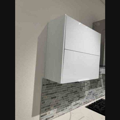 White kitchen cabinet mounted on wall above a tiled backsplash and stove.