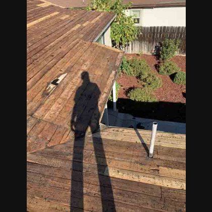 Shadow of a person on a damaged wooden roof, revealing exposed underlayment.