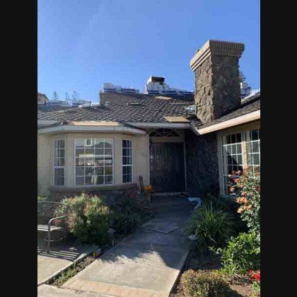 Home with a partially torn roof, a stone chimney, and a concrete walkway.