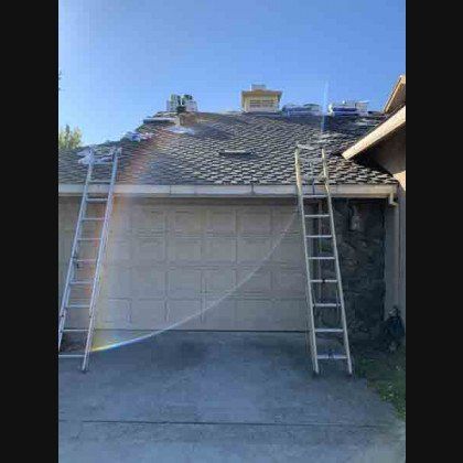 Two ladders leaning against a house roof, where roof tiles are being replaced, garage in front.