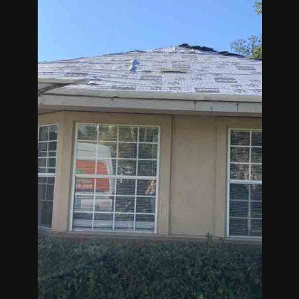 House with damaged roof and large windows under a clear sky.