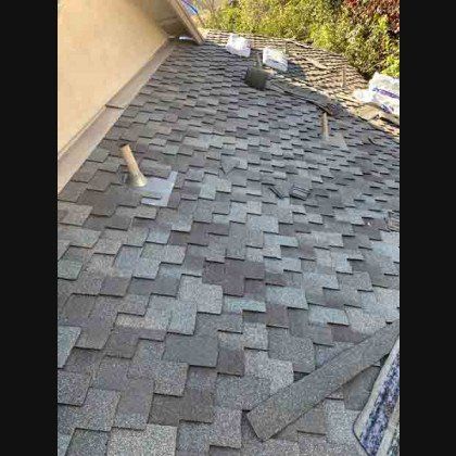 A partially shingled roof with dark gray shingles being installed.  A trowel and vent are visible.