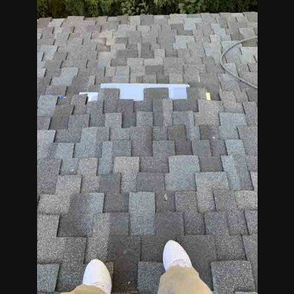 Person standing on asphalt shingle roof, looking down at a gap with exposed roofing underlayment.