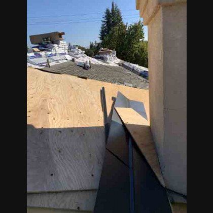Roof construction with plywood, dark metal flashing, and partial roof. Sunny day.