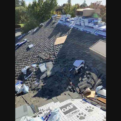 Roof being repaired; shingles, underlayment, and materials scattered across surface. Daytime, sunny outdoors.