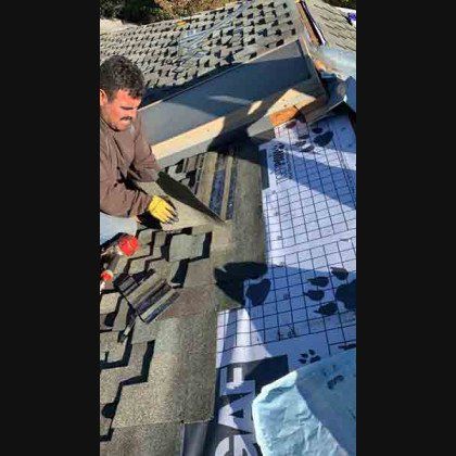 Roofer in brown shirt and yellow gloves, on a roof replacing shingles, sunny day.