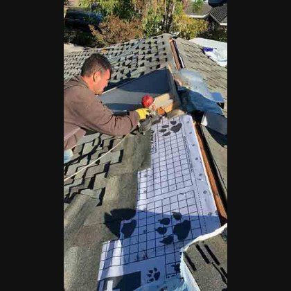 Roofer using a mallet on a roof. Sunlight, dark shingles, blue underlayment.