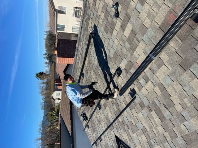 A worker installs solar panel rails on a residential rooftop under a blue sky.