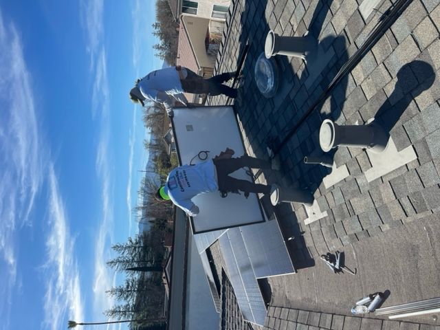 Two workers installing solar panels on a rooftop under a blue sky.