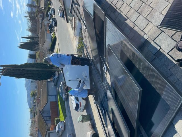 Two workers installing solar panels on a rooftop in a residential neighborhood.