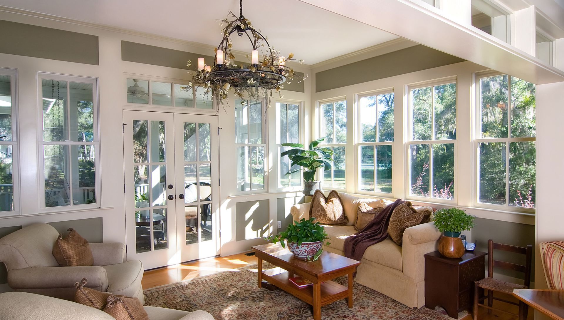 Sunroom with white trim, windows, French doors, beige sofas, coffee table, and chandelier.