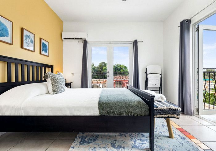 Bedroom with black bed, yellow accent wall, and balcony overlooking greenery.