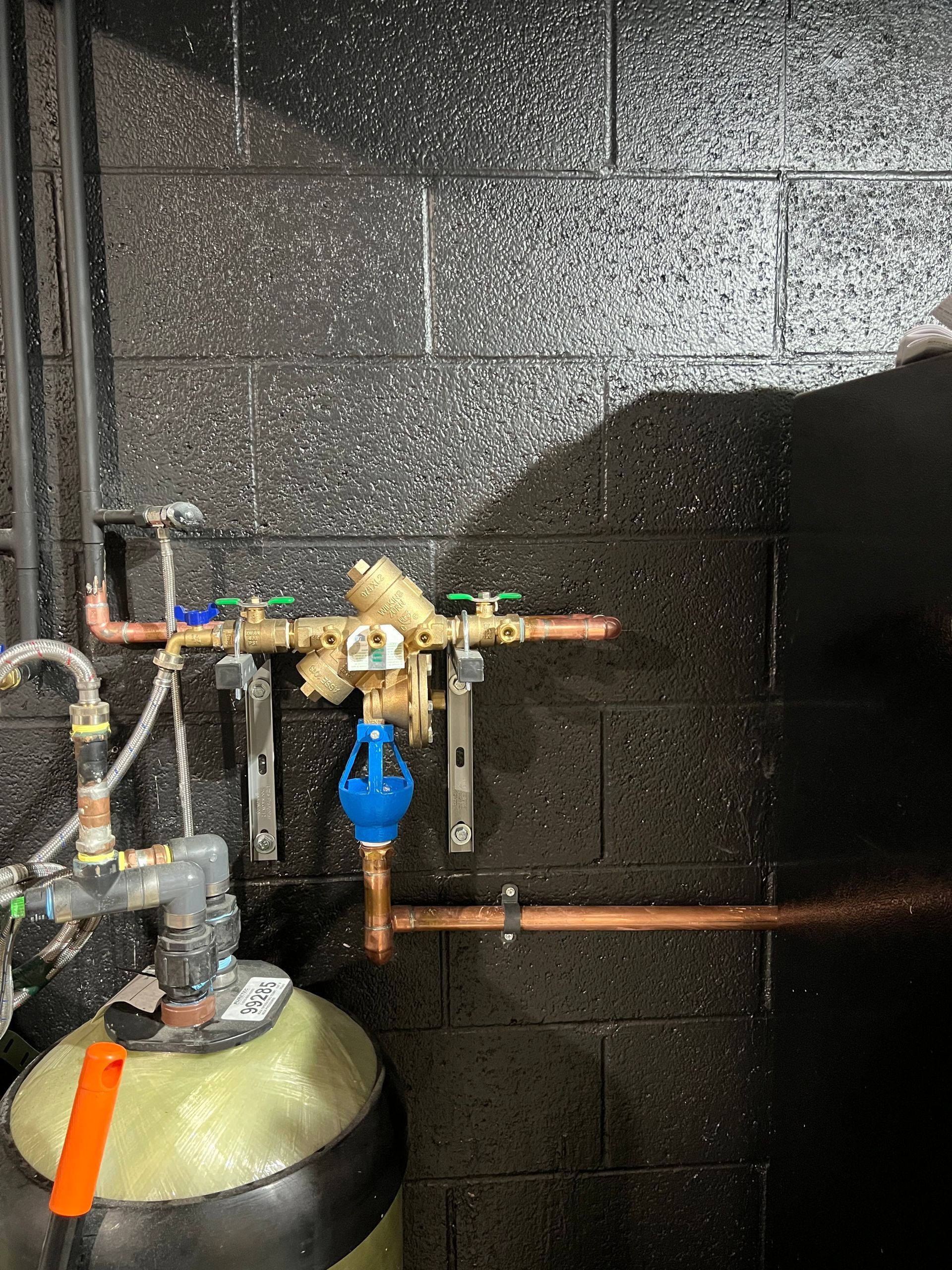 a black brick wall with copper pipes and a valve that says ' a ' on it