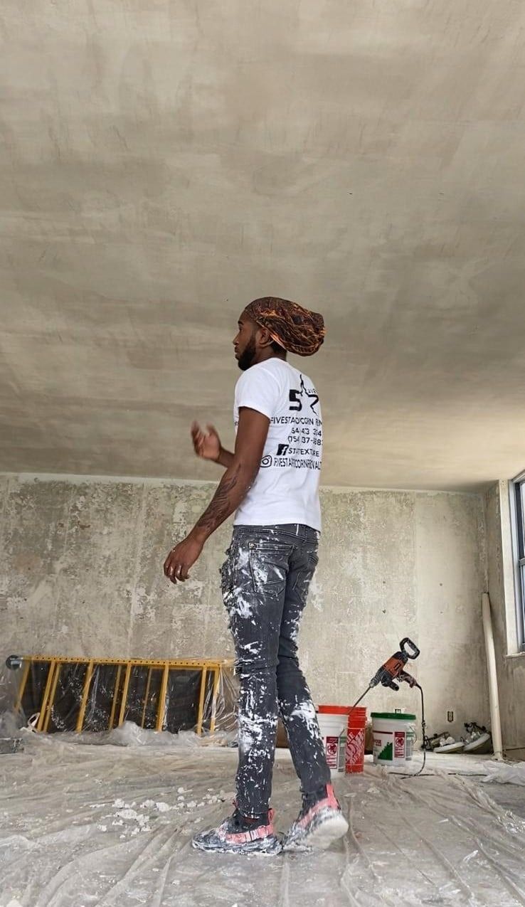 Person painting an unfinished room, standing near a wall with tools and paint supplies nearby.