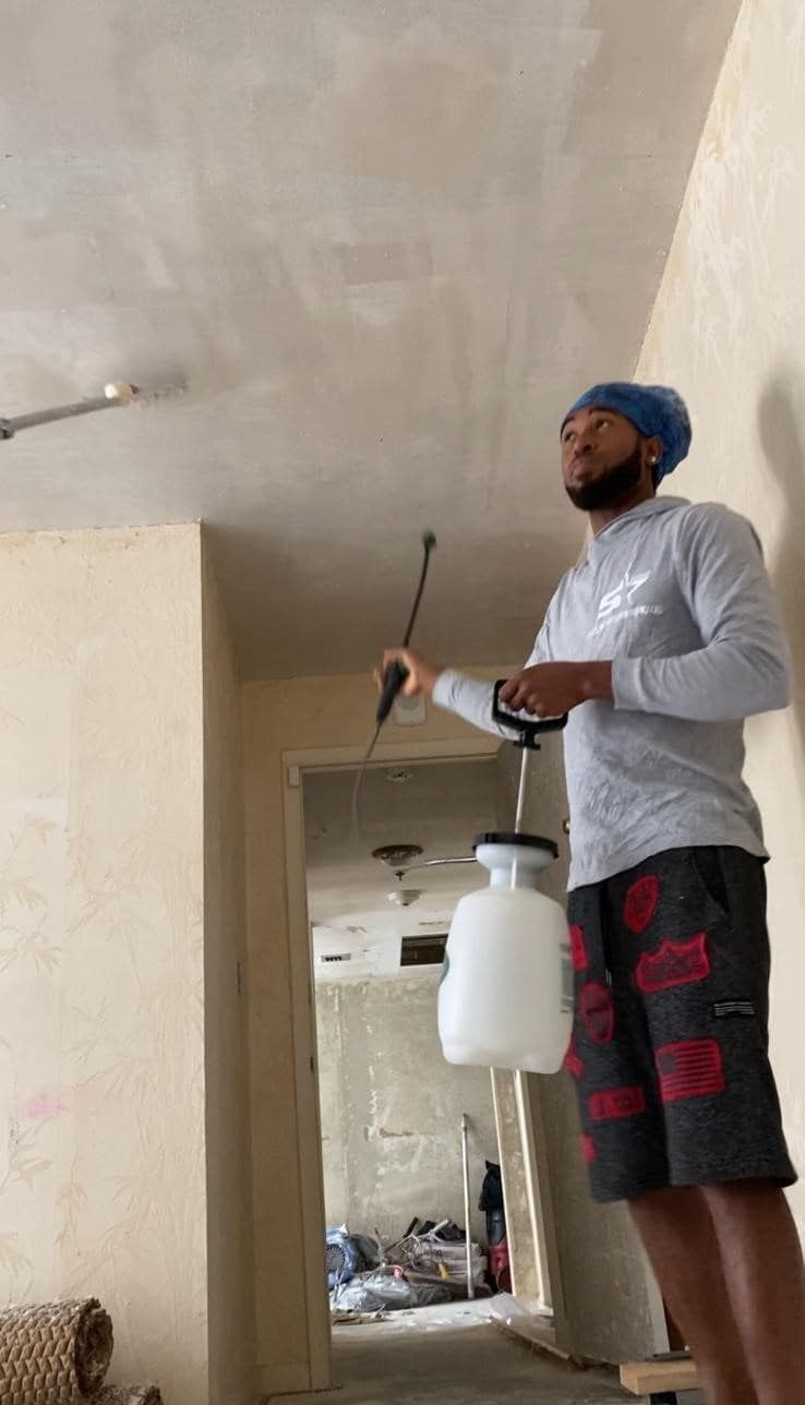 Person spraying paint with a white sprayer in an unfinished room during renovation