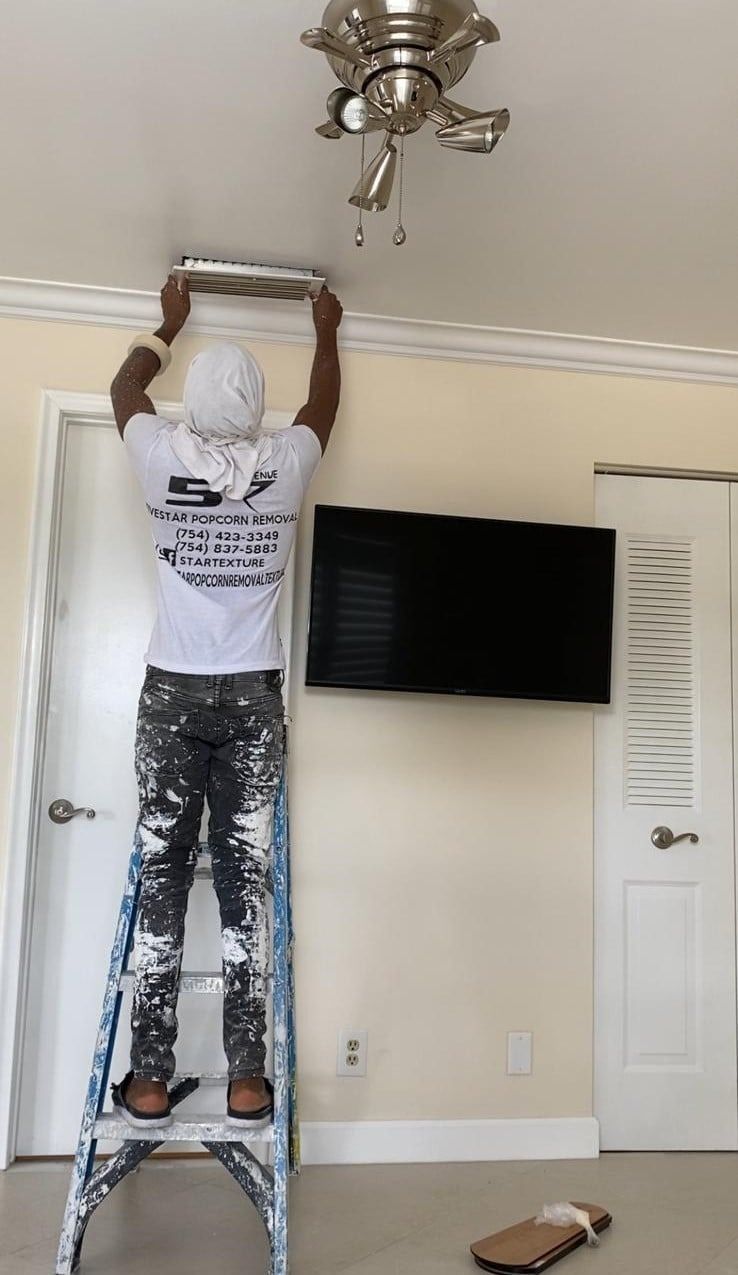 Person on a ladder reaching up to a ceiling light fixture in a living room