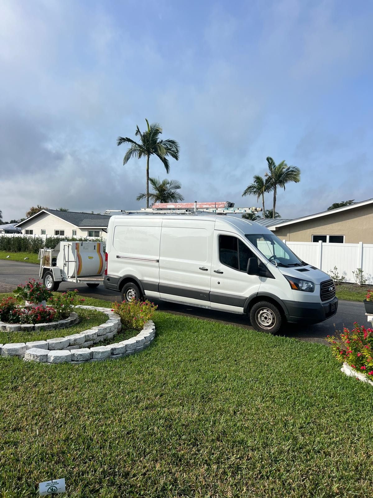 White cargo van towing a small trailer on a grassy curbside in a suburban neighborhood