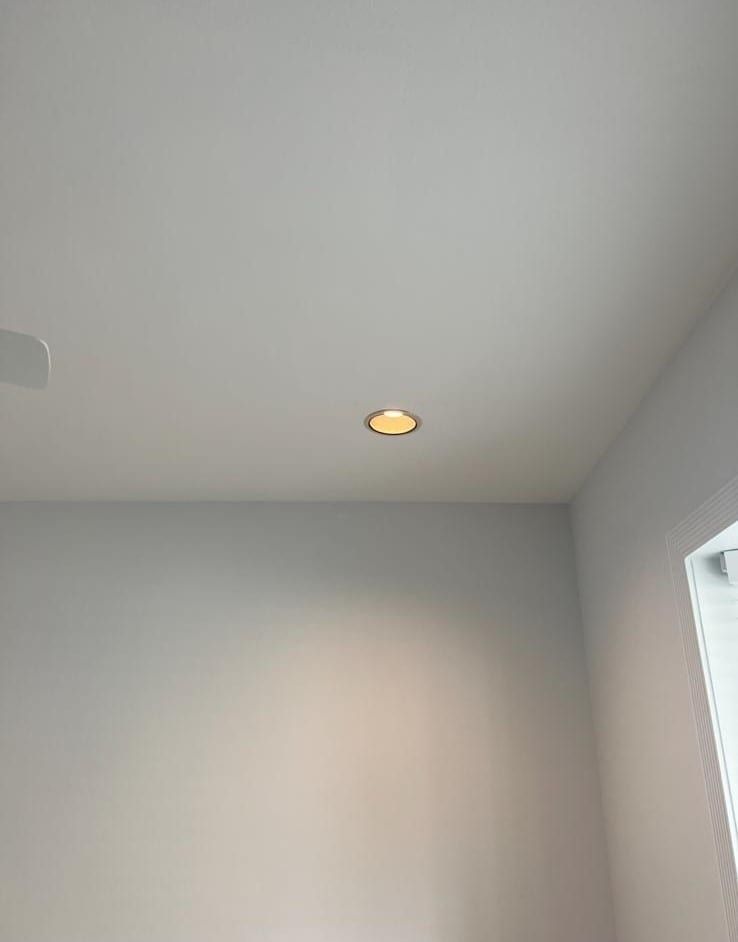 Ceiling corner of a room with a small recessed light and light gray walls.