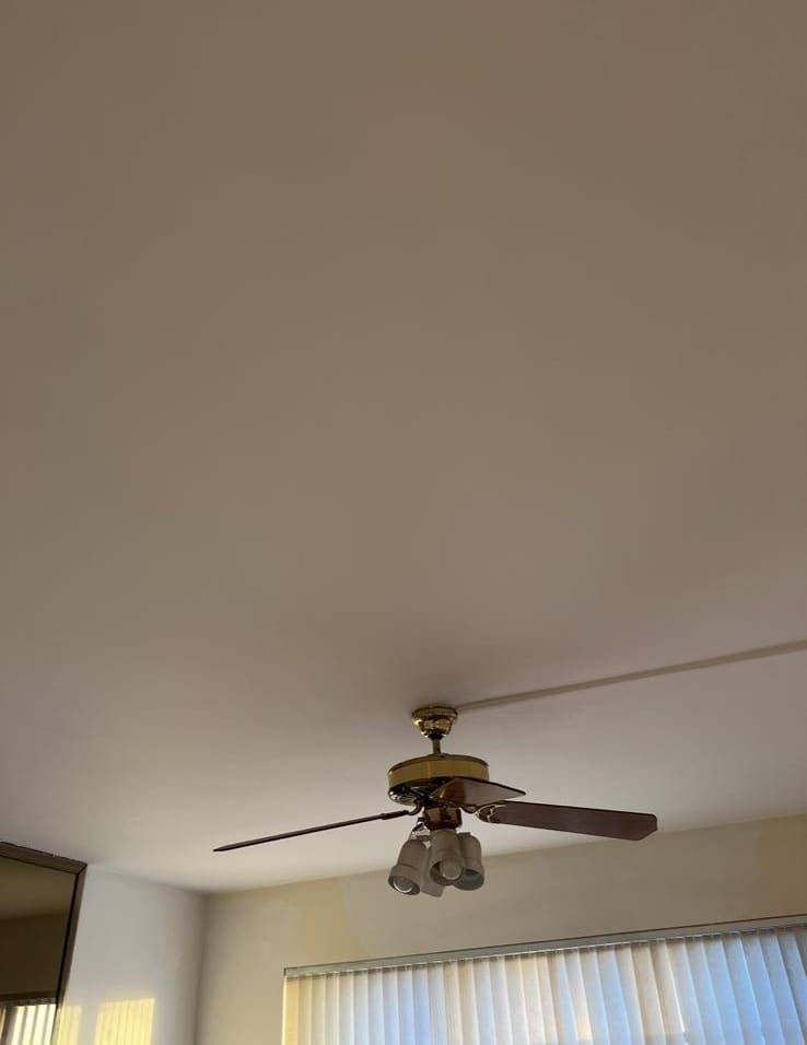 Ceiling fan with light fixture above a window with vertical blinds in a room