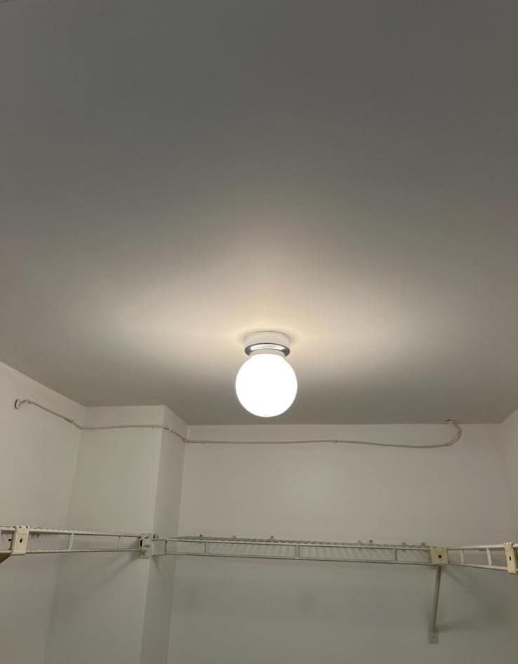 White room ceiling with a lit round bulb and wall-mounted shelves below