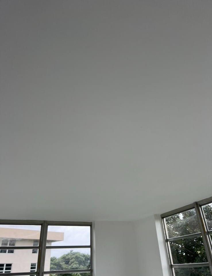 White ceiling in a room with large windows showing nearby buildings and trees outside.