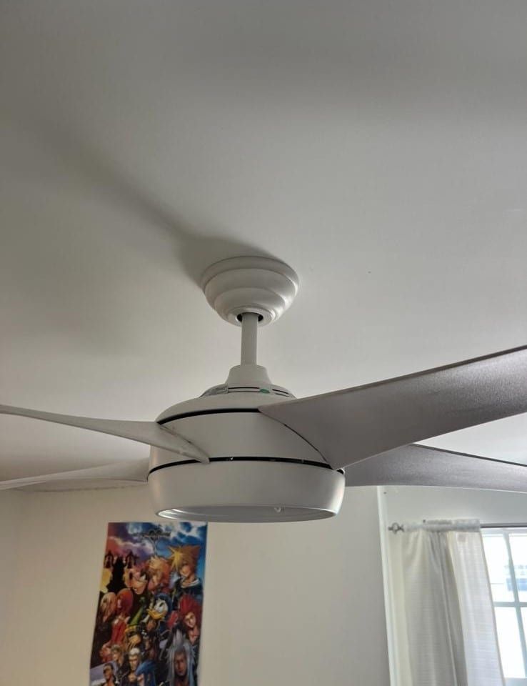 White ceiling fan with dark blades in a room near a window and colorful wall art