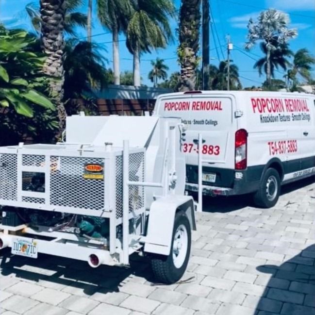 White utility trailer and van labeled “Popcorn Removal” parked on a sunny paved lot with palm trees.