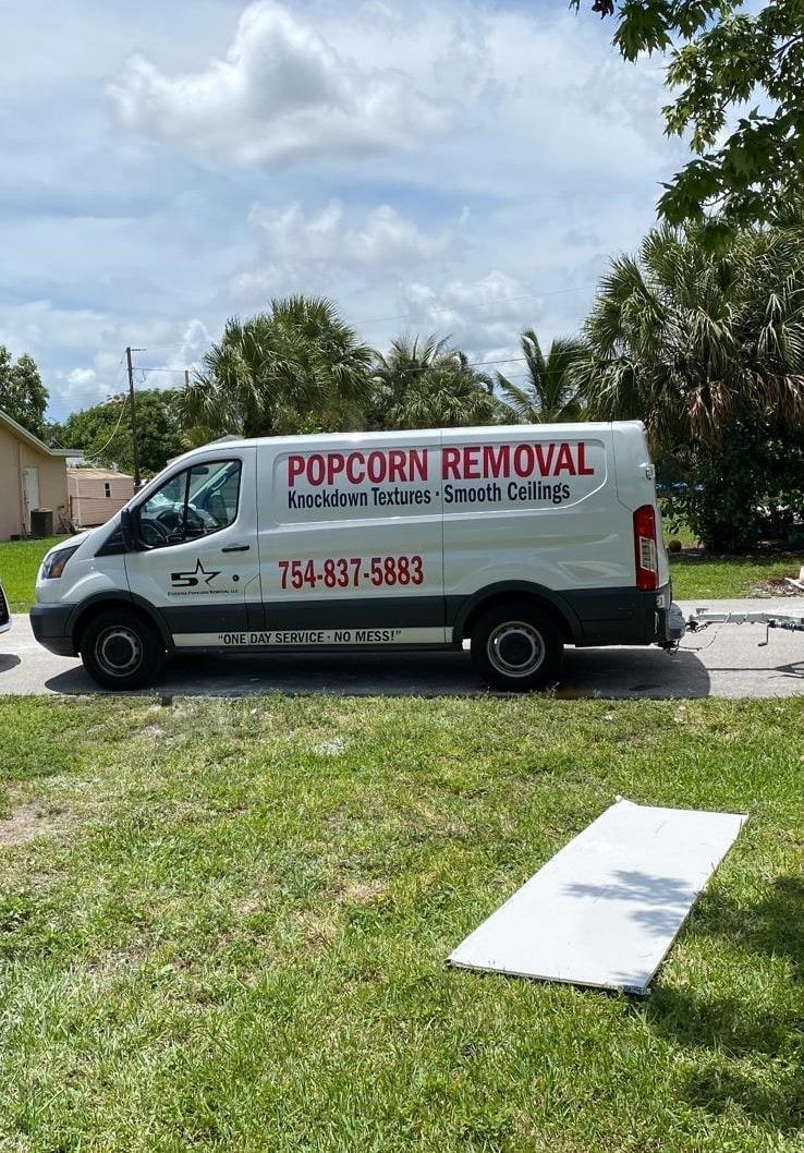 White popcorn removal van parked by a grassy yard, with a fallen white board in the foreground.