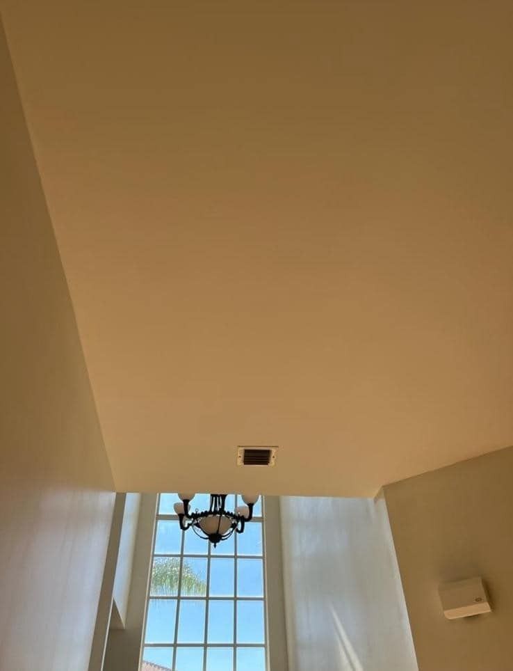 High ceiling and window with sheer curtains, chandelier, and a wall sconce in a bright room