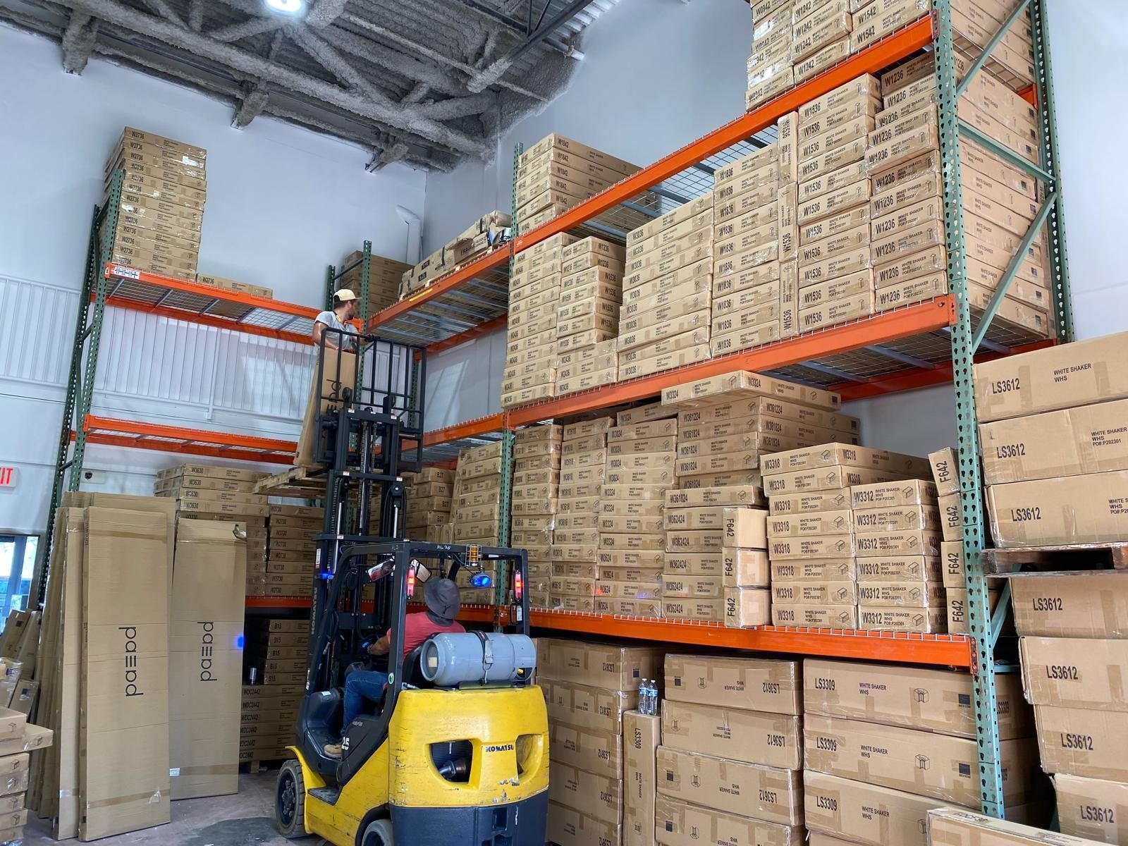 Warehouse aisle with stacked boxes on tall racks and a yellow forklift in the foreground