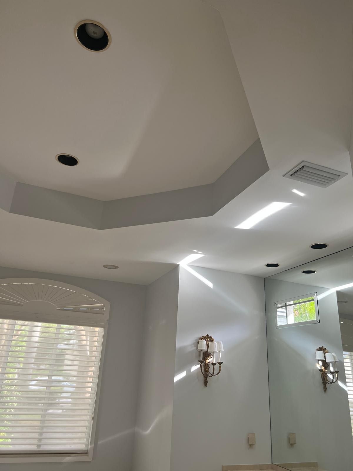 Bright white bathroom with skylights, blinds, wall sconces, and a patterned ceiling.