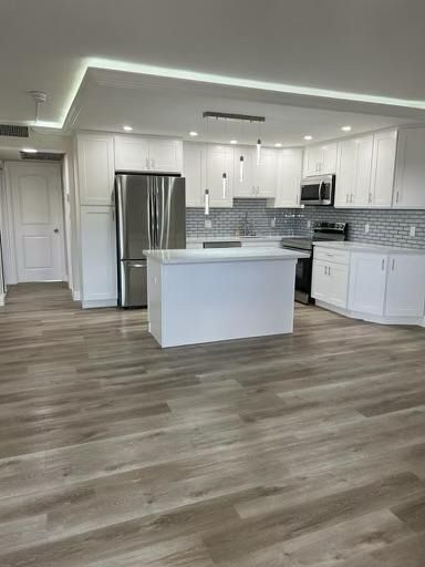 Bright modern kitchen with white cabinets, stainless steel appliances, island, and wood-look flooring
