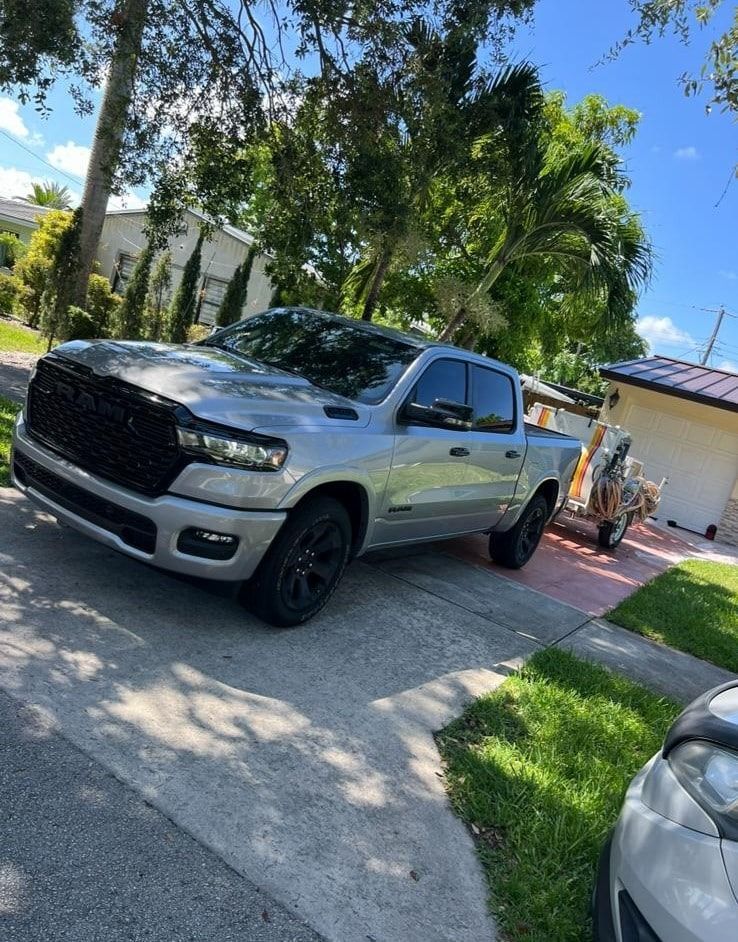 Silver pickup truck parked in a sunny driveway with palm trees and a house in the background