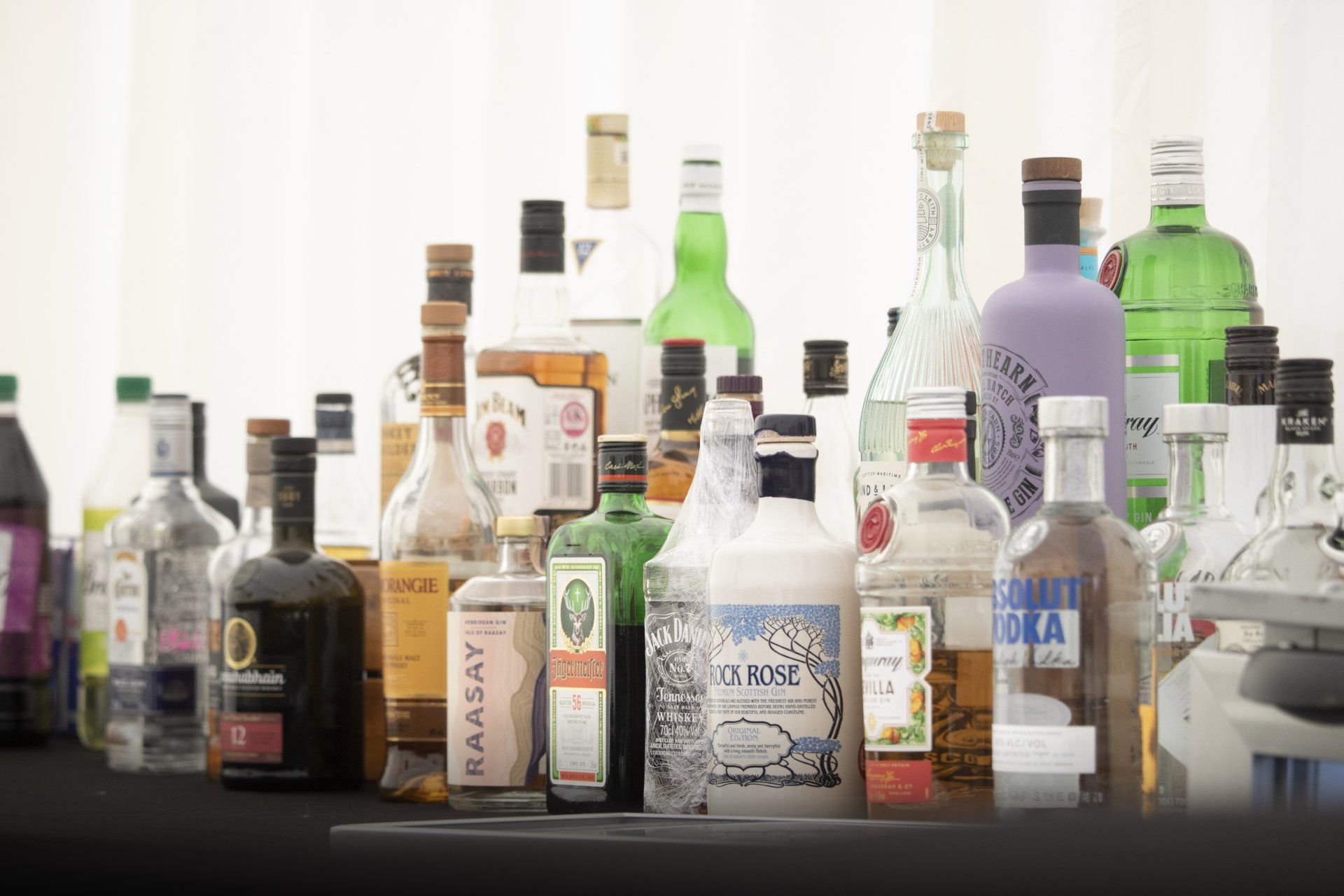 Many bottles of liquor are lined up on a table including a bottle of kaasay